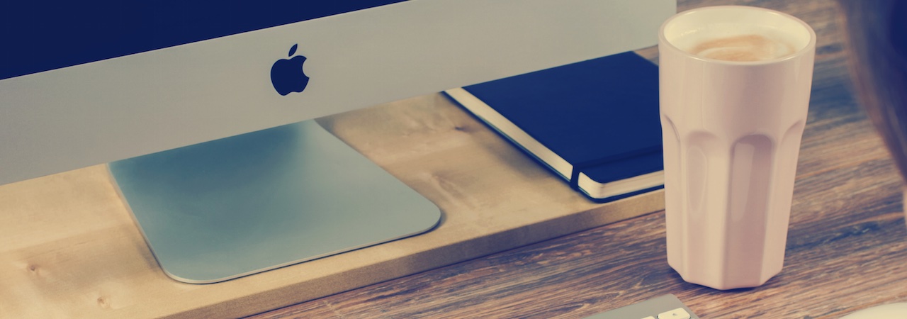 close up of a desk with an iMac, phone and a cup with coffee in it.