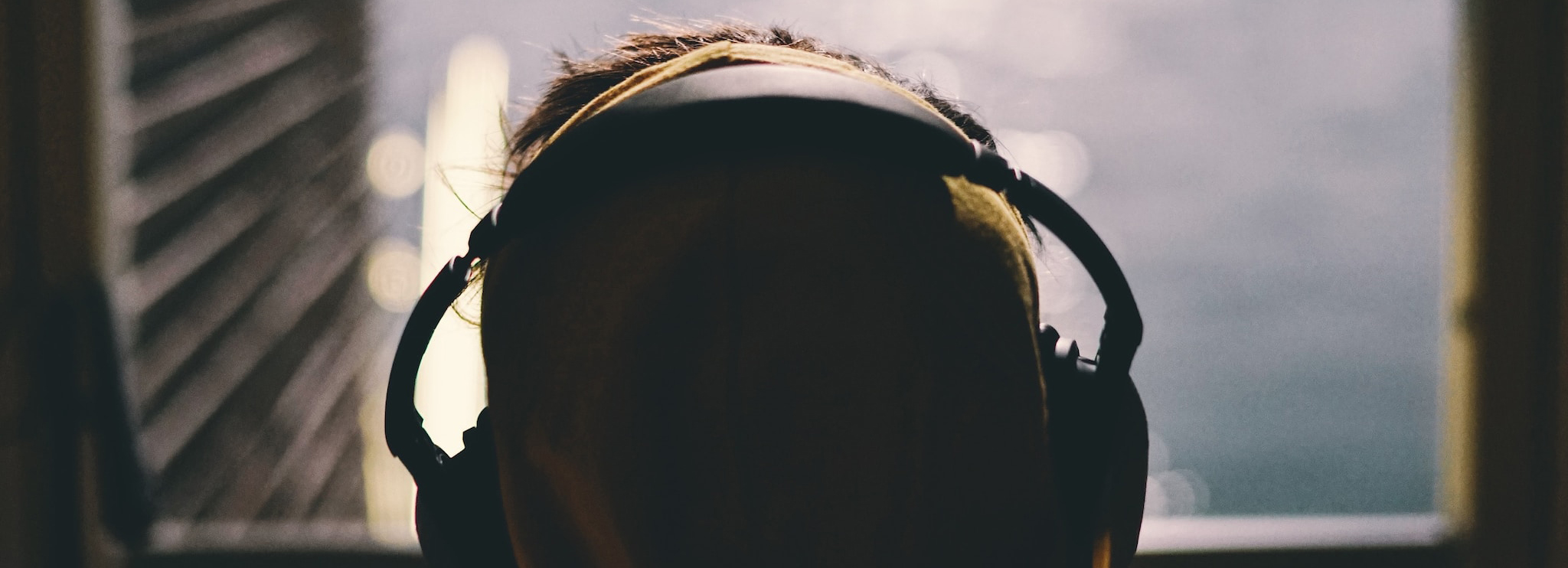 Silhouette of a person wearing noise-canceling headphones while sitting in front of a window. Meant to signify one possible accommodation for effectively working with neurodivergent team members.